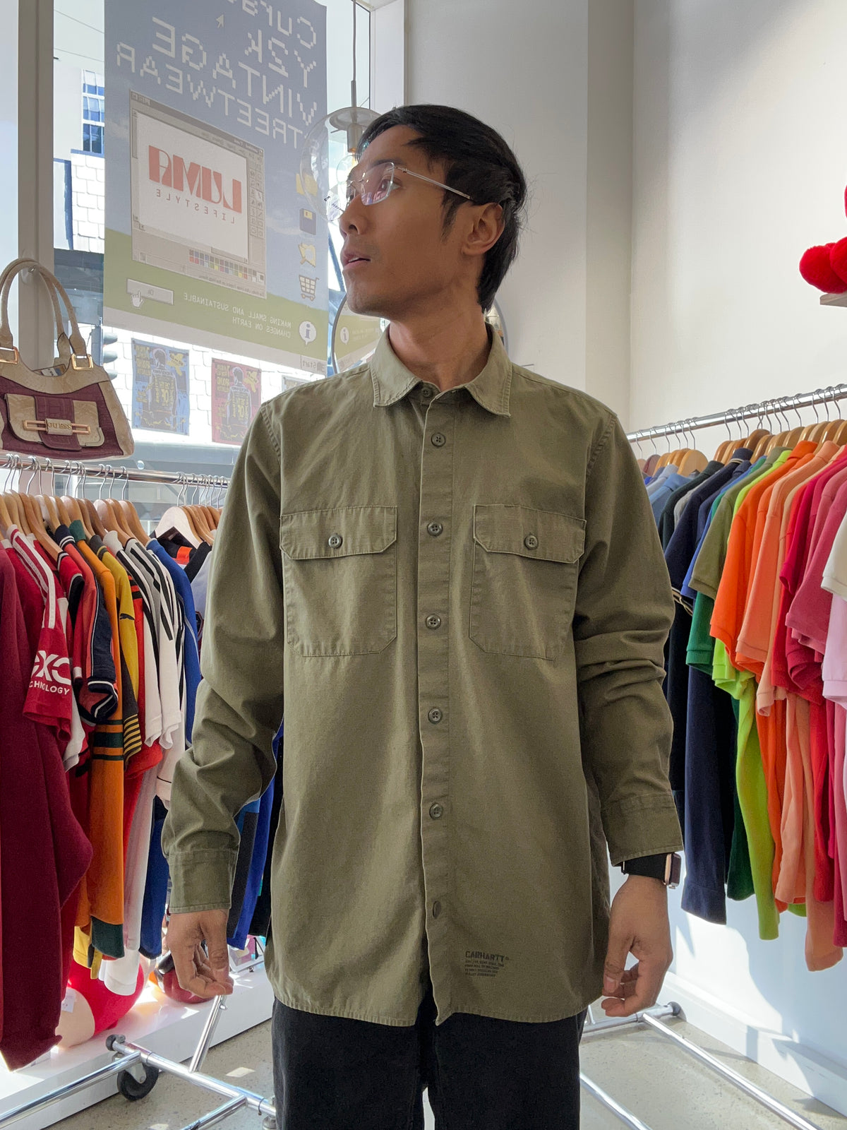 WIP olive green Carhartt long-sleeve work shirt with dual chest pockets and a small tag detail at the lower hem Large