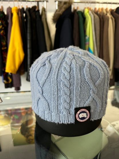 light blue or grey cable-knit wool beanie featuring a Canada Goose arctic disc logo patch on the front