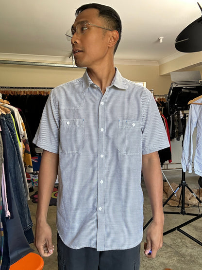 short-sleeve button-up shirt from the brand Stüssy, featuring a classic hickory stripe pattern and dual chest pockets.Medium
