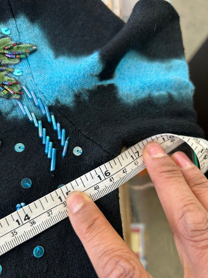 black knit sweater features blue tie-dye accents and floral embroidery with beaded details.