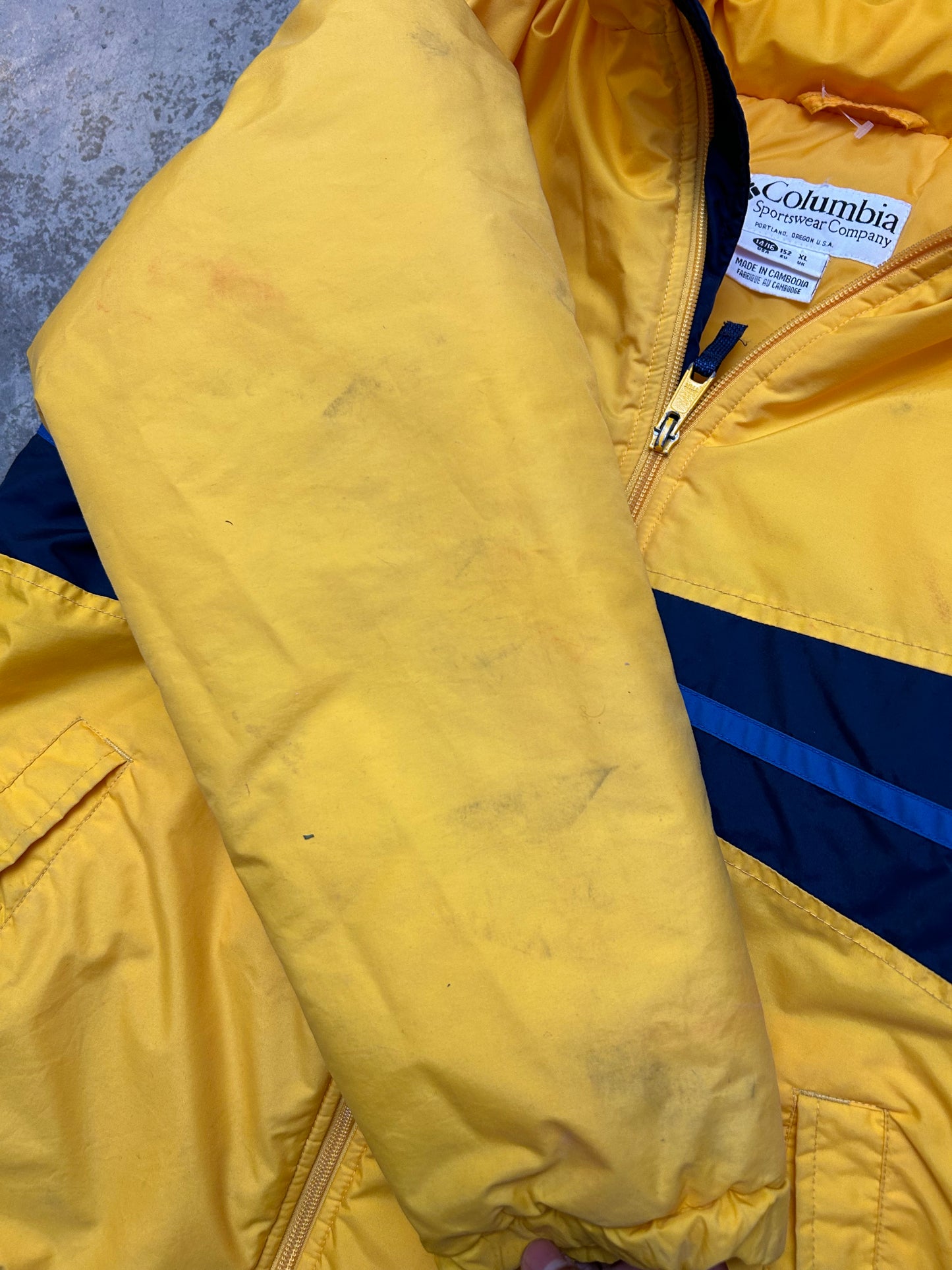 Medium vintage yellow Columbia Sportswear jacket with a blue stripe design across the chest. Has Stains