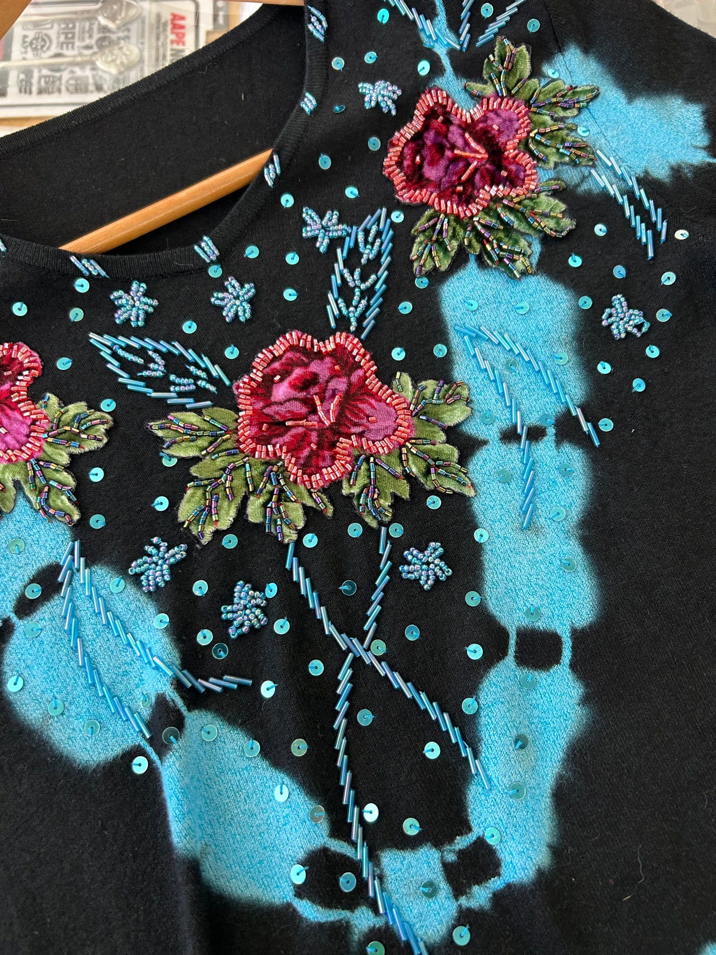 black knit sweater features blue tie-dye accents and floral embroidery with beaded details.