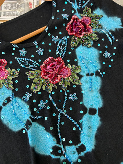 black knit sweater features blue tie-dye accents and floral embroidery with beaded details.