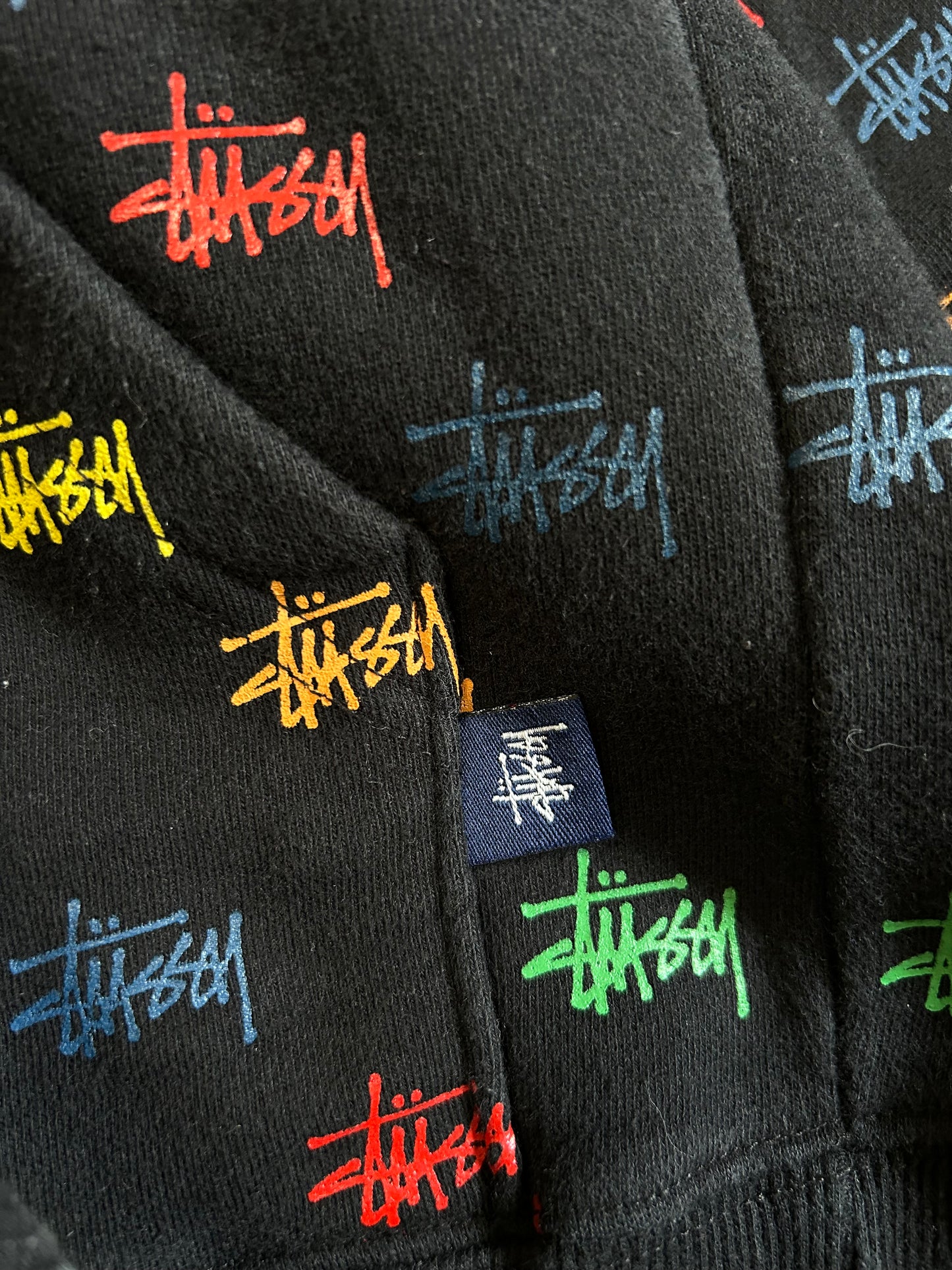 black, pullover-style hoodie featuring an all-over, multi-colored Stüssy logo print Small