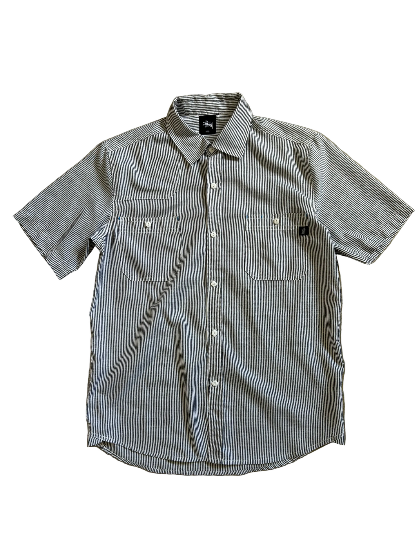short-sleeve button-up shirt from the brand Stüssy, featuring a classic hickory stripe pattern and dual chest pockets.Medium