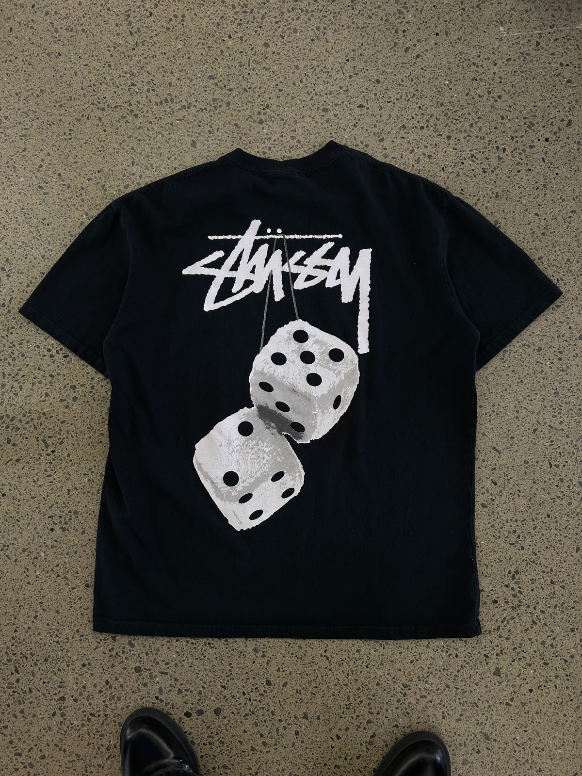 Stüssy Fuzzy Dice Tee in black, featuring a prominent fuzzy dice graphic on the back. Large