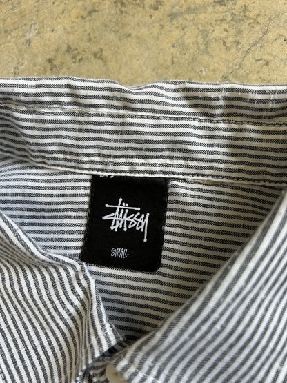 short-sleeve button-up shirt from the brand Stüssy, featuring a classic hickory stripe pattern and dual chest pockets.Medium